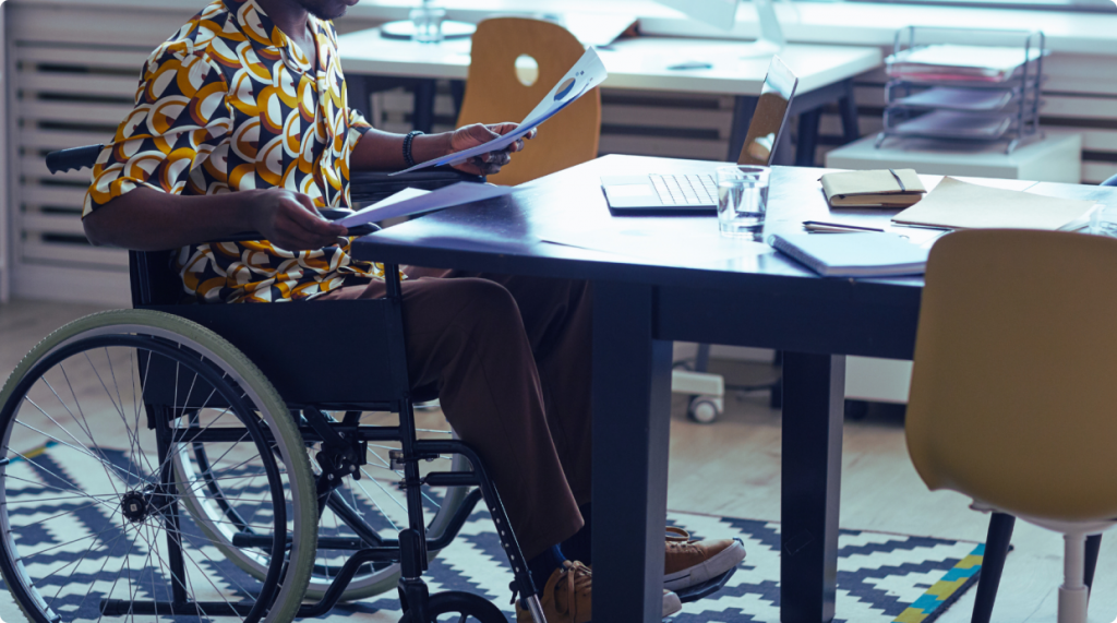 Person in a wheelchair working at a desk, holding documents, in a modern office setting, highlighting accessibility