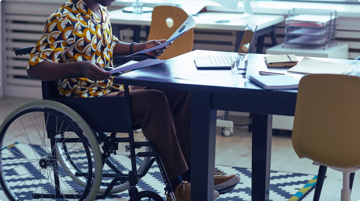 Person in a wheelchair working at a desk, holding documents, in a modern office setting, highlighting accessibility 